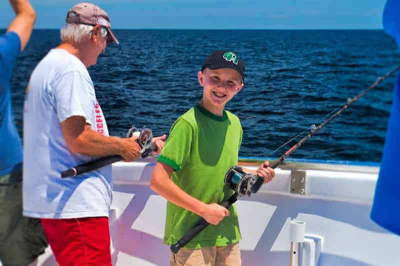 A smiling young boy poses with a fishing rod on a boat. 